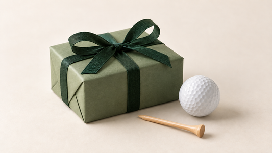 Geburtstagsgeschenk für Golfer: salbeigrüne Geschenkbox mit dunkelgrüner Schleife, weißem Golfball und Holztee.
